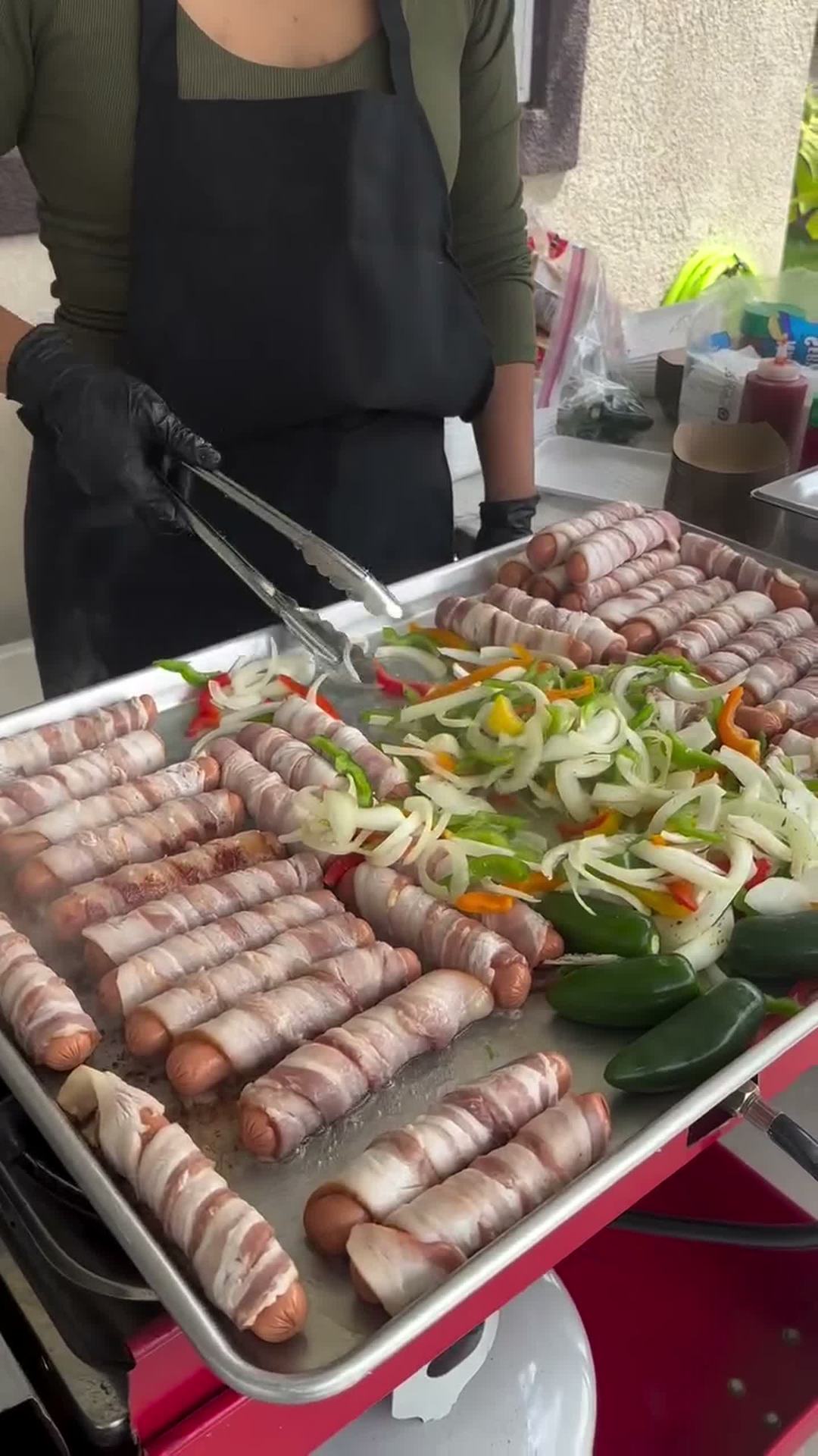 Bacon-wrapped hot dog being built fresh on the grill